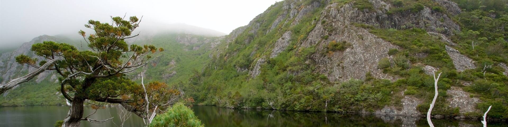 Un lago sereno rodeado de colinas verdes exuberantes y una montaña imponente al fondo.