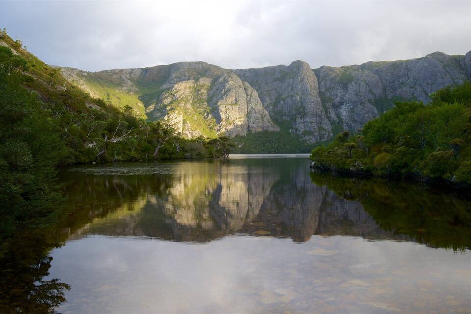 A calm lake reflecting mountains and dense greenery.