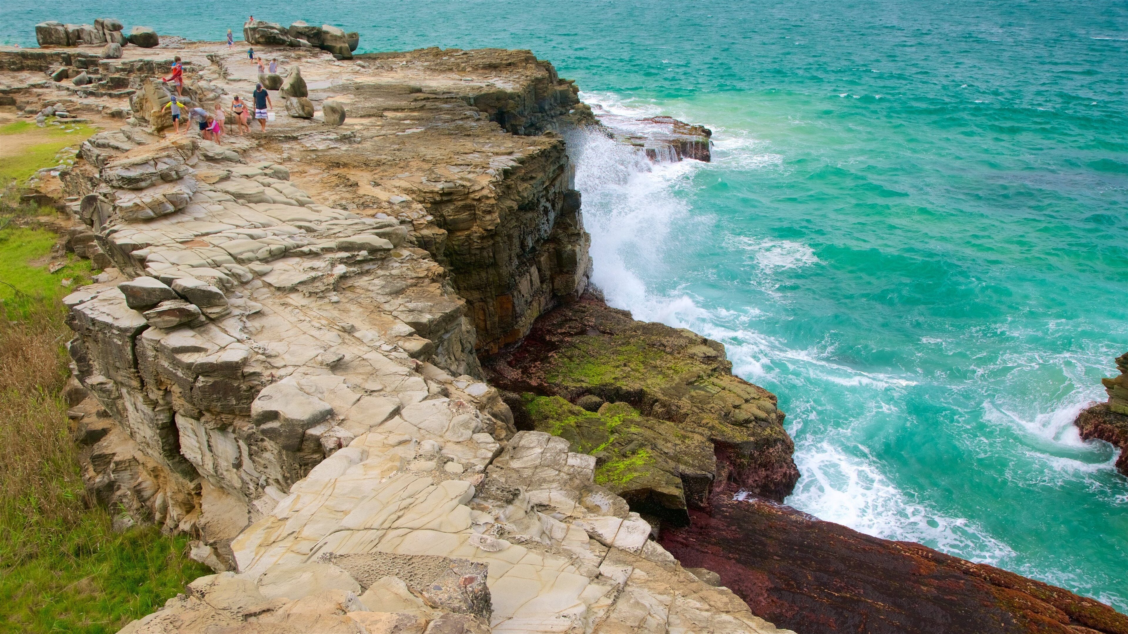 A rocky coastline with a waterfall and people walking along the edge.
