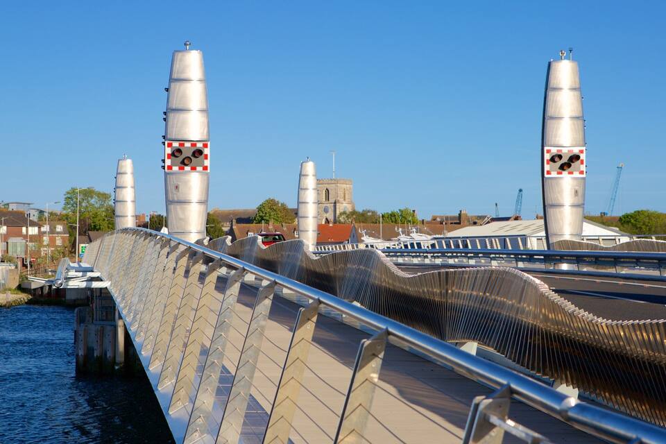 A bridge with a distinctive ribbed design, a body of water beneath, and a church in the background.