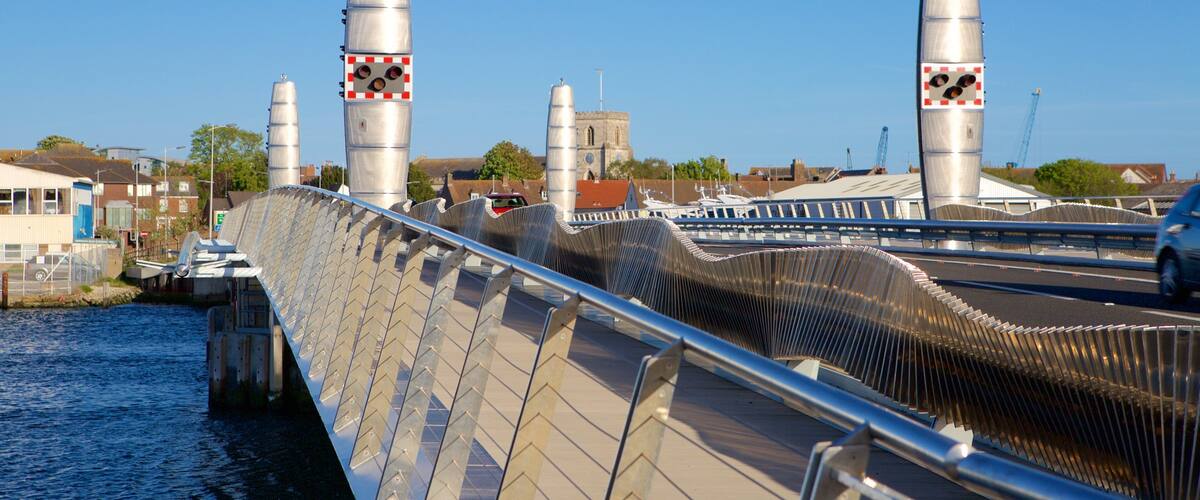 A bridge with a distinctive ribbed design, a body of water beneath, and a church in the background.