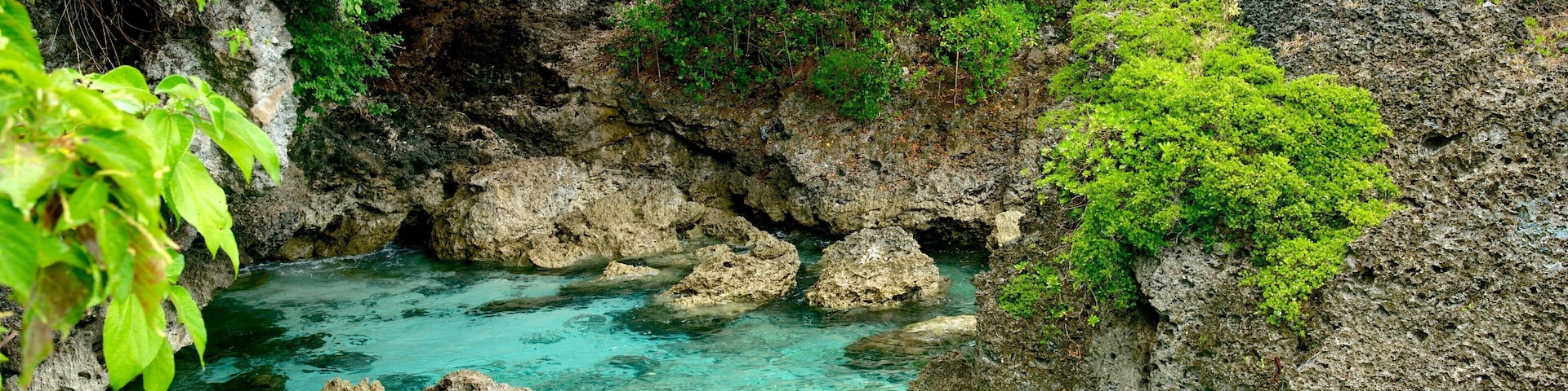 A clear turquoise stream surrounded by rocky cliffs and lush greenery.