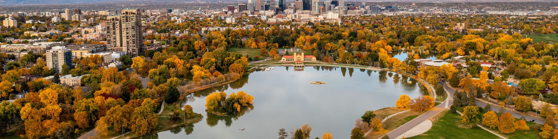 A cityscape with autumn foliage, a central lake, and distant mountains.