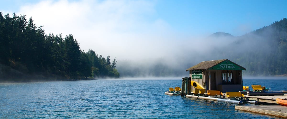 A boat rental station on a calm lake surrounded by forested hills.