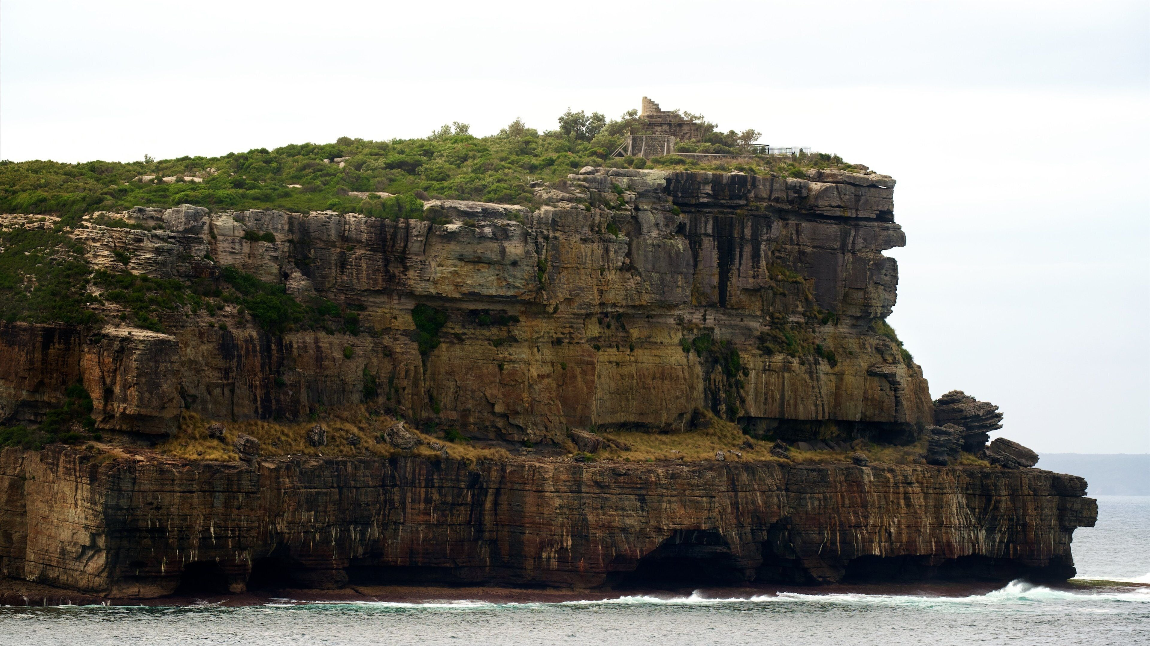 A large rock formation with a small building on top, surrounded by greenery and overlooking the ocean.