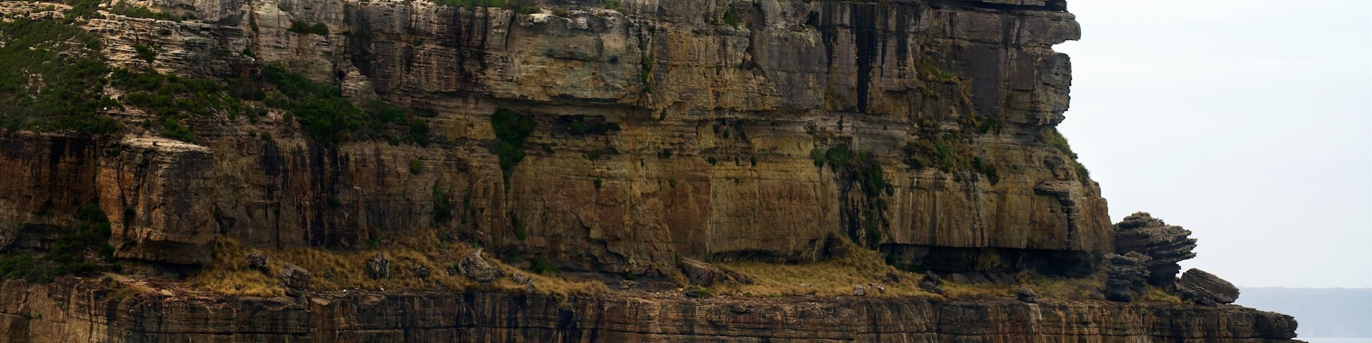 Una gran formación rocosa con un edificio pequeño en la cima, rodeada de vegetación y con vistas al océano.