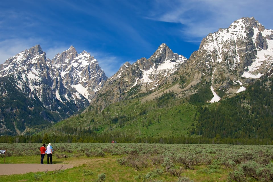 A mountainous landscape with snow-capped peaks, a clear sky, and a path with two people walking.