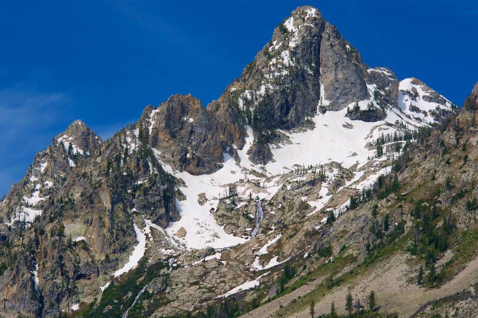 A rugged mountain peak with snow patches and a clear blue sky.