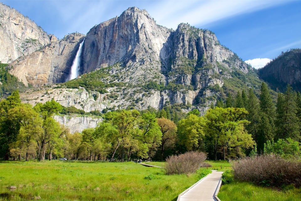 A waterfall cascading down a rocky mountain, surrounded by lush greenery and a clear sky.