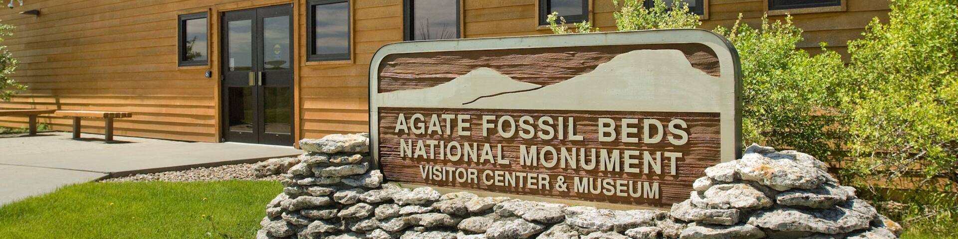 A wooden building with a sign for the Agate Fossil Beds National Monument Visitor Center & Museum.
