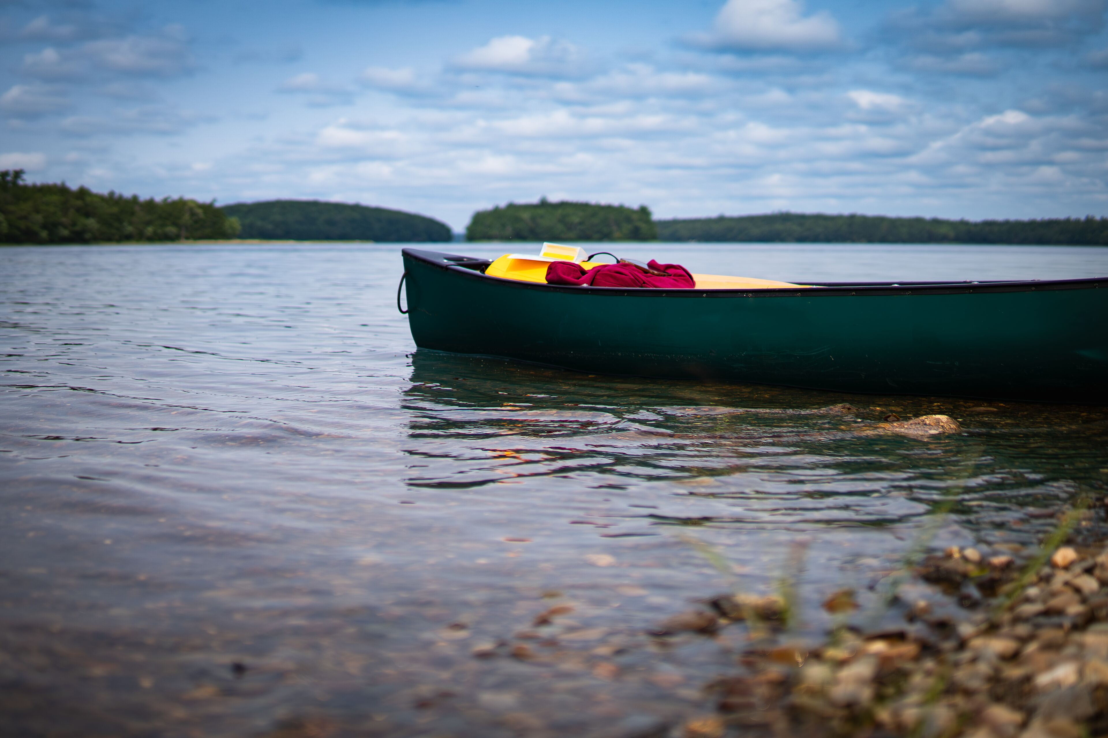A green canoe with yellow and red items on the shore of a calm lake.