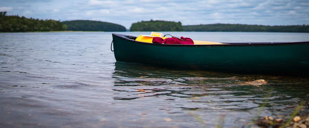 A green canoe with yellow and red items on the shore of a calm lake.