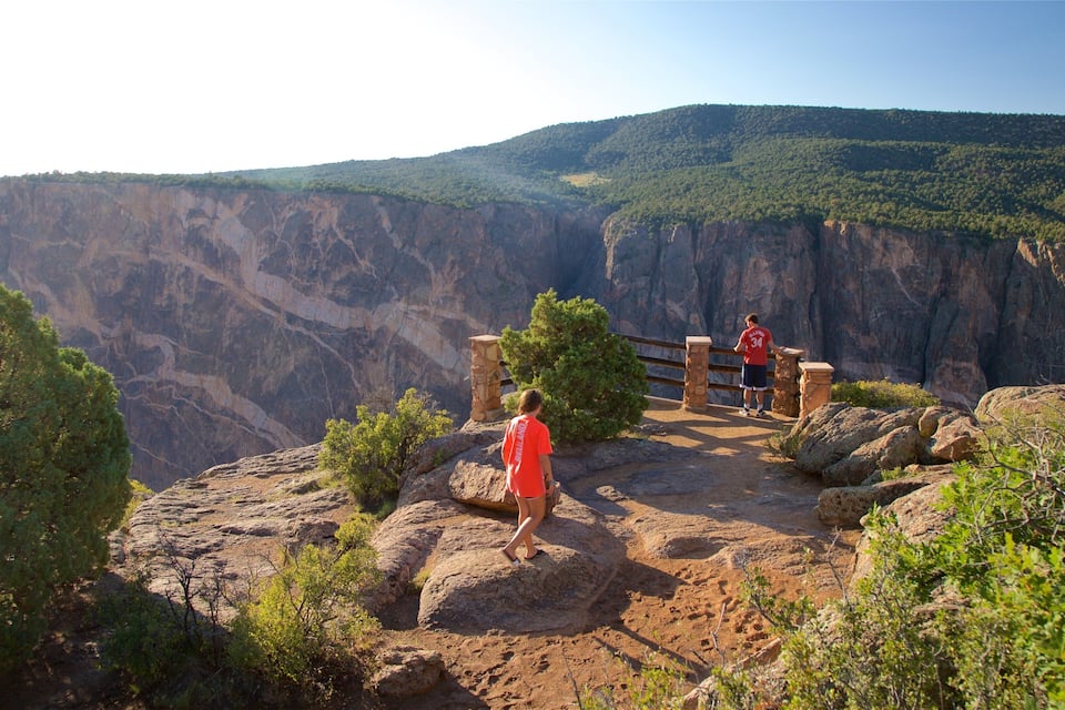 A person in a red shirt standing on a rocky outcrop overlooking a canyon with a wooden viewing platform.