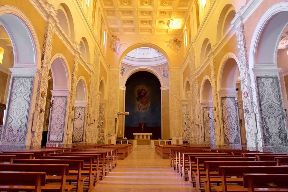 Interior de uma igreja com bancos de madeira, colunas de mármore e um altar central.