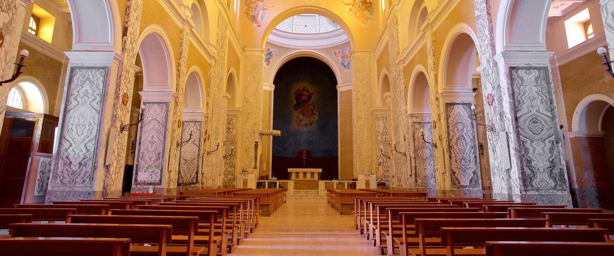 An interior of a church with wooden pews, marble columns, and a central altar.