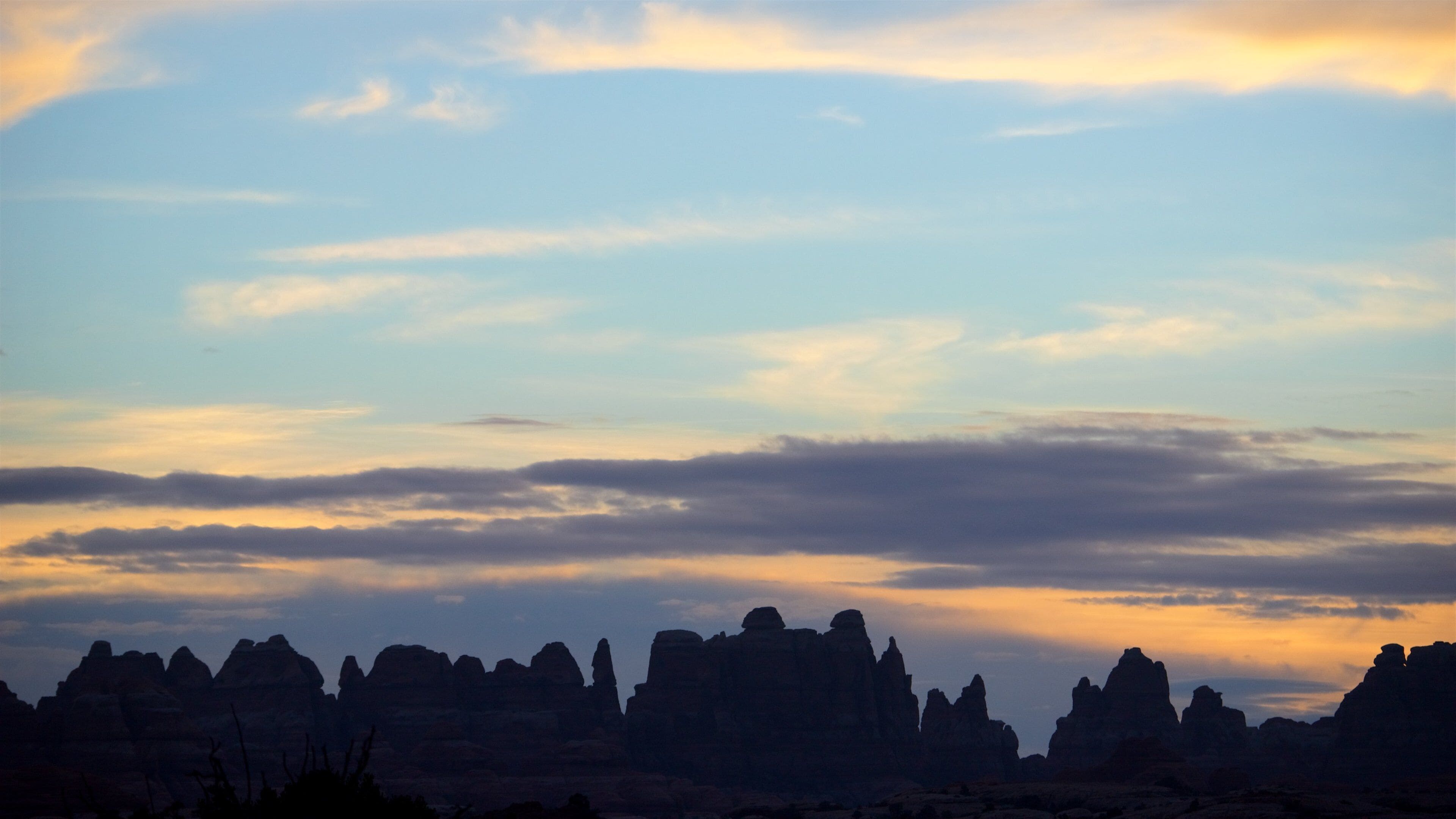 A desert landscape with rock formations silhouetted against a sunset sky.