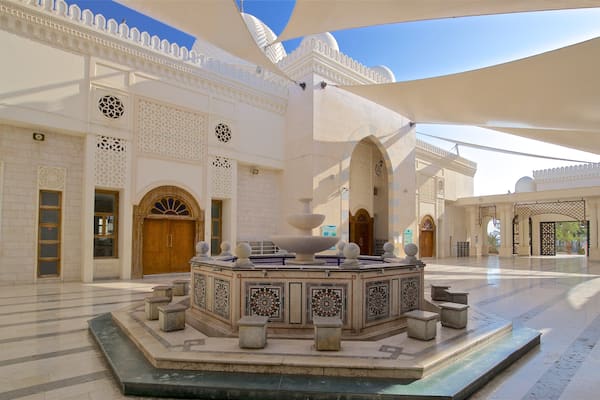 An ornate courtyard with a central fountain, intricate wall designs, and a large arched entrance.