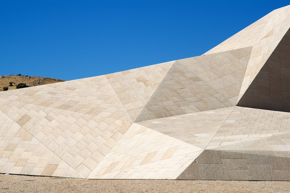 A modern architectural structure with geometric patterns and a clear blue sky in the background.