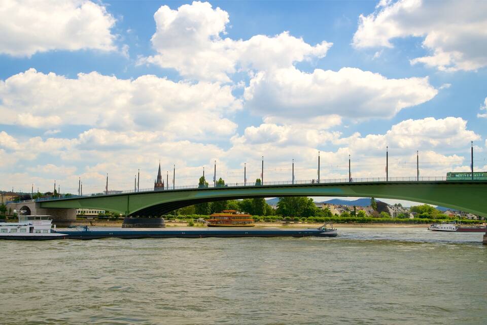 Un pont vert enjambant une rivière, avec des bateaux, une église et une voie ferrée.