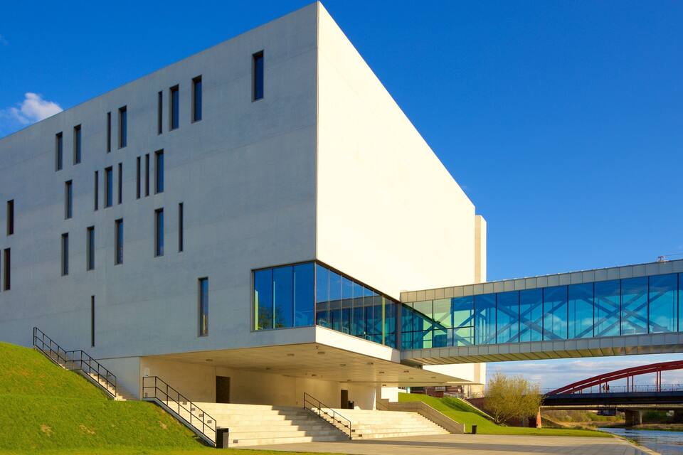 A modern building with a flat roof, large windows, and a staircase leading to the entrance.