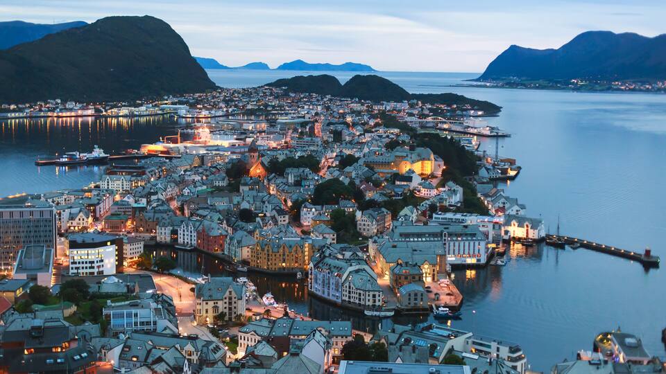 A coastal town with a harbor, historic buildings, and mountains in the background.