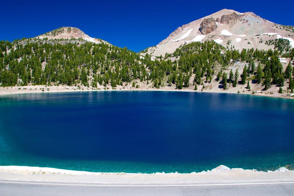 A clear blue lake surrounded by mountains and dense forests.