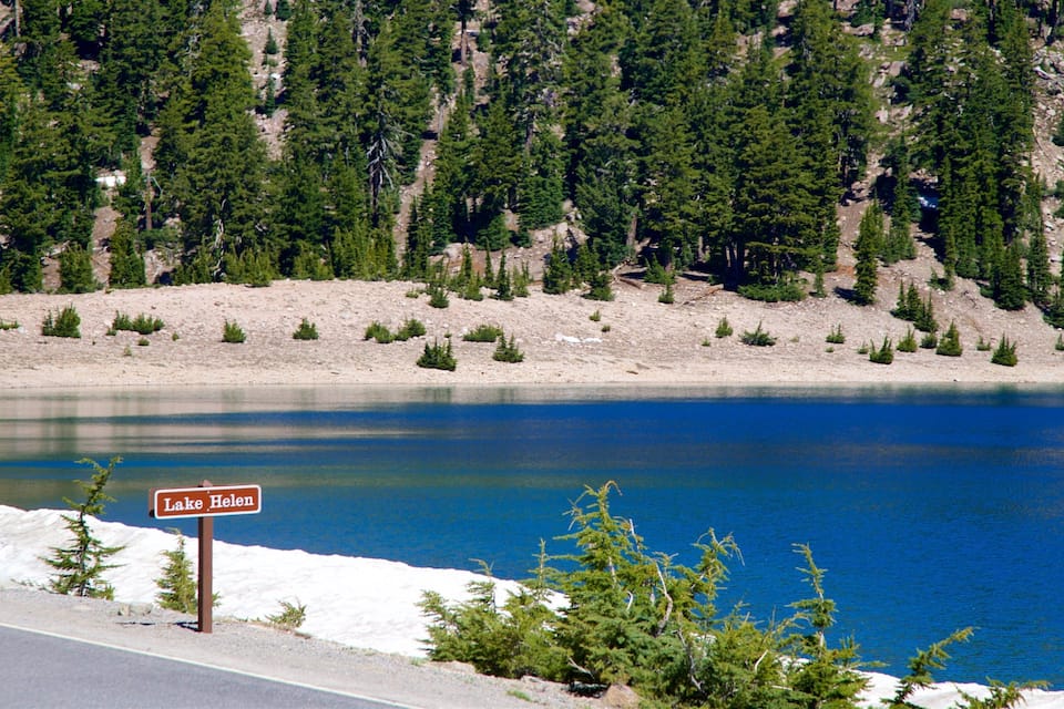 A lake with a sign reading "Lake Helen" surrounded by dense forest and rocky terrain.