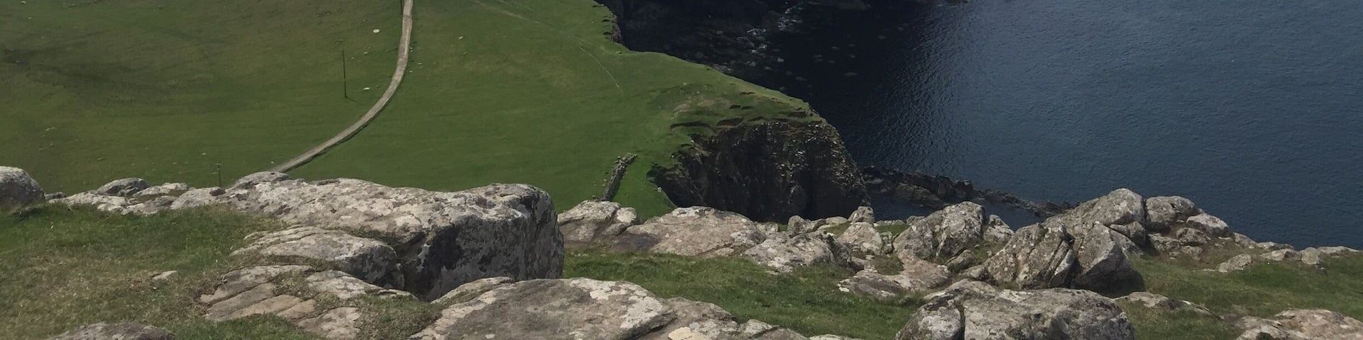 A coastal landscape with a grassy path leading to a lighthouse on a cliff.