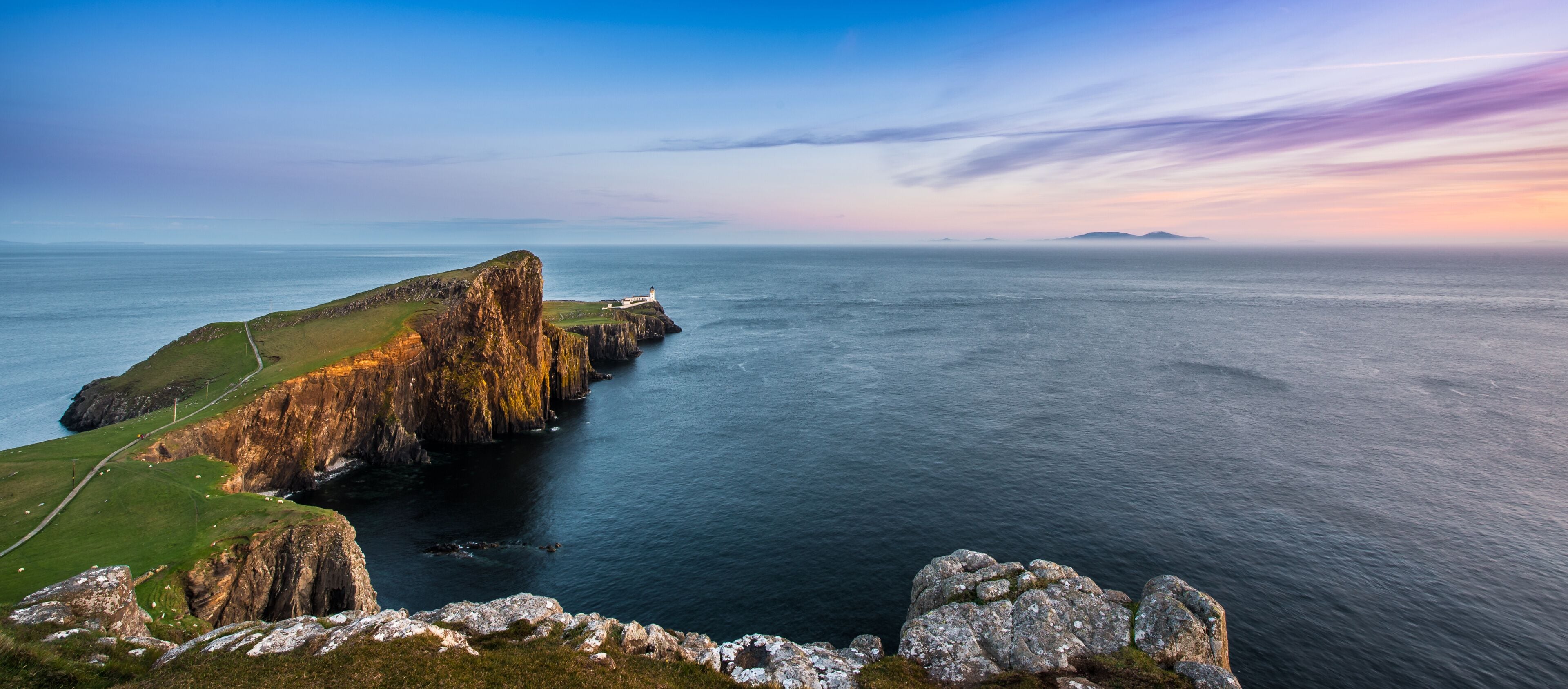 A coastal landscape with a prominent cliff, a lighthouse, and a distant island.