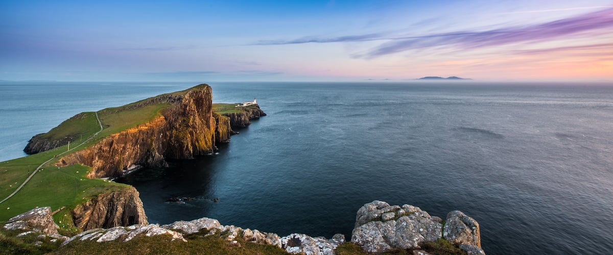 A coastal landscape with a prominent cliff, a lighthouse, and a distant island.