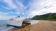 A sailboat named 'Zunile' beached on a sandy shore with a forested hill in the background.