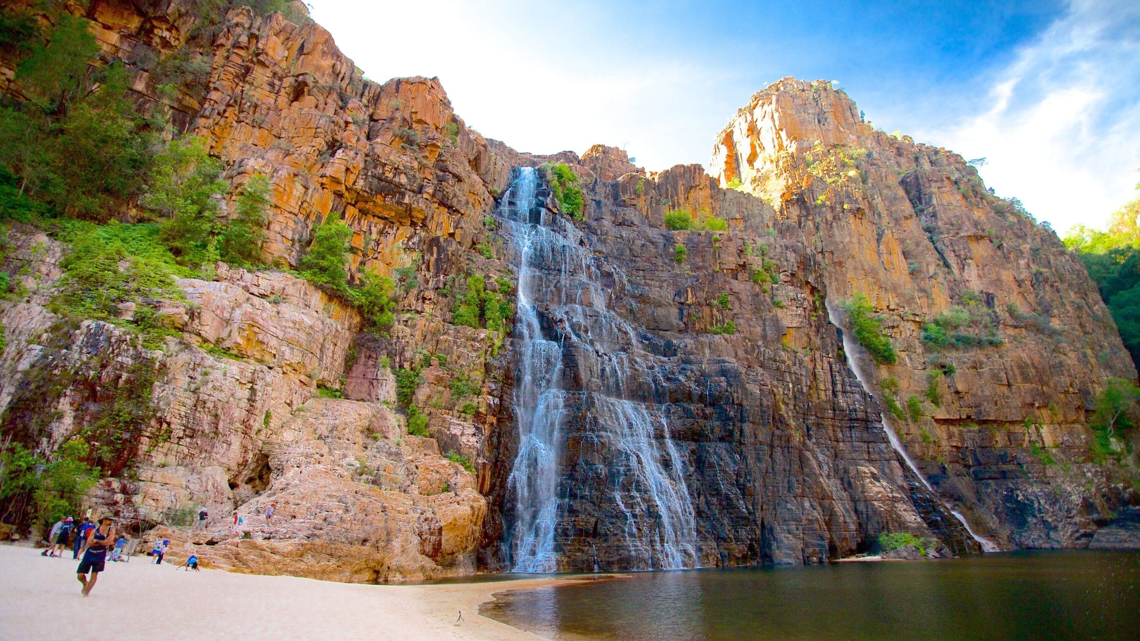A waterfall cascading down a rocky cliff into a calm pool at a beach.