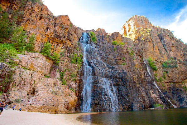 A waterfall cascading down a rocky cliff into a calm pool at a beach.