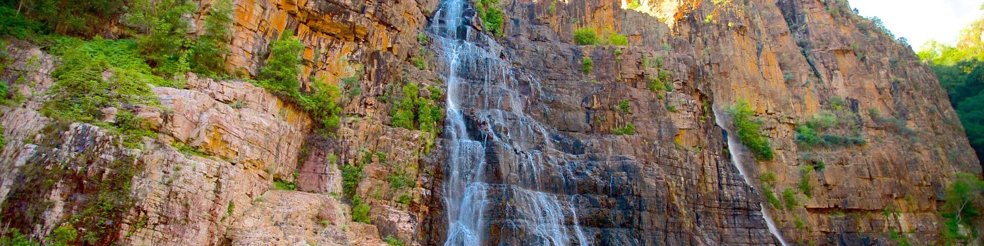 Una cascada se precipita por un acantilado rocoso hacia una piscina tranquila en la playa.