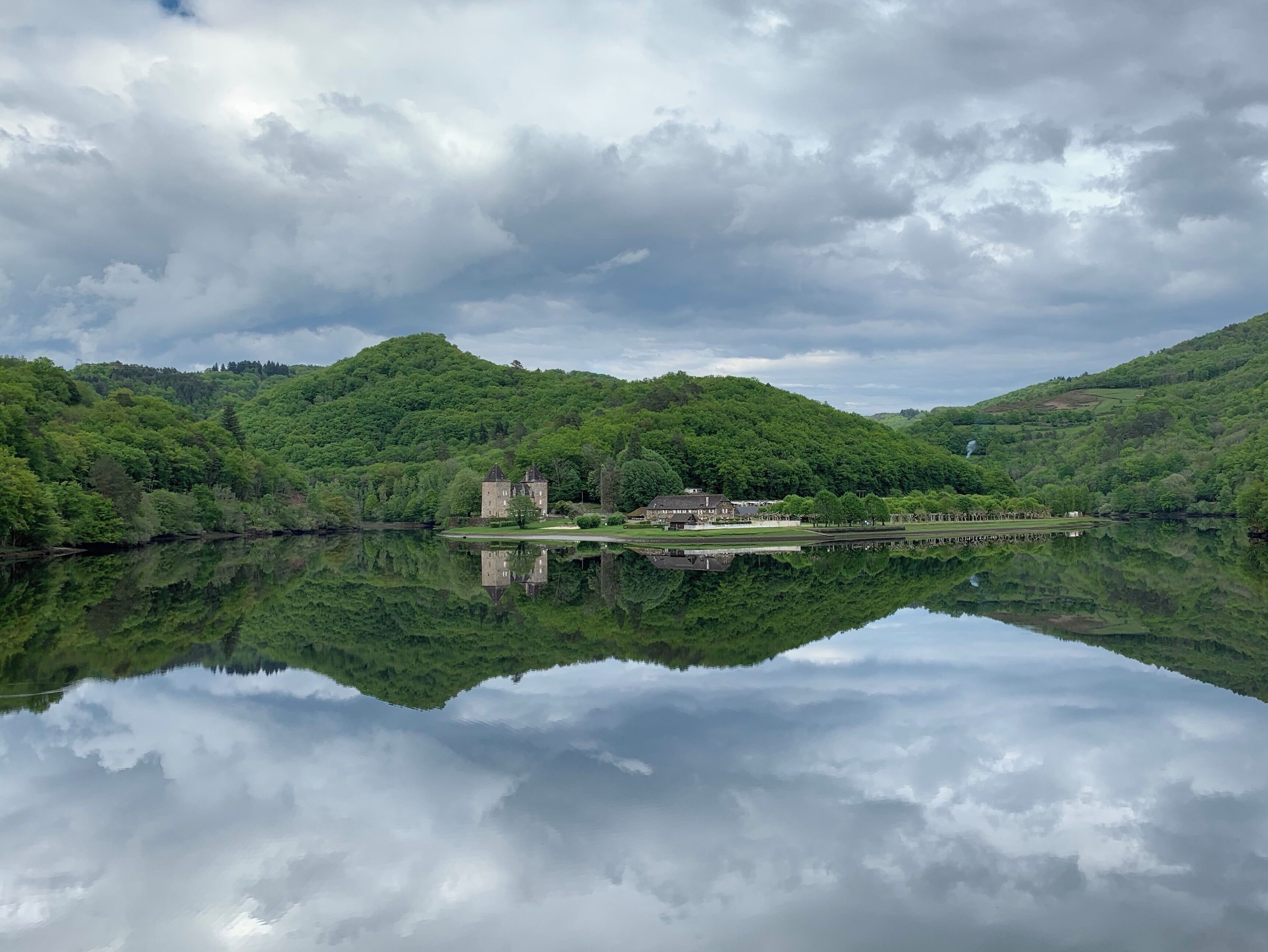 A castle on a hill with a lake reflecting the sky and trees.
