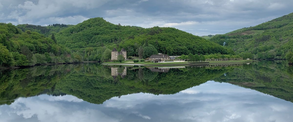 A castle on a hill with a lake reflecting the sky and trees.