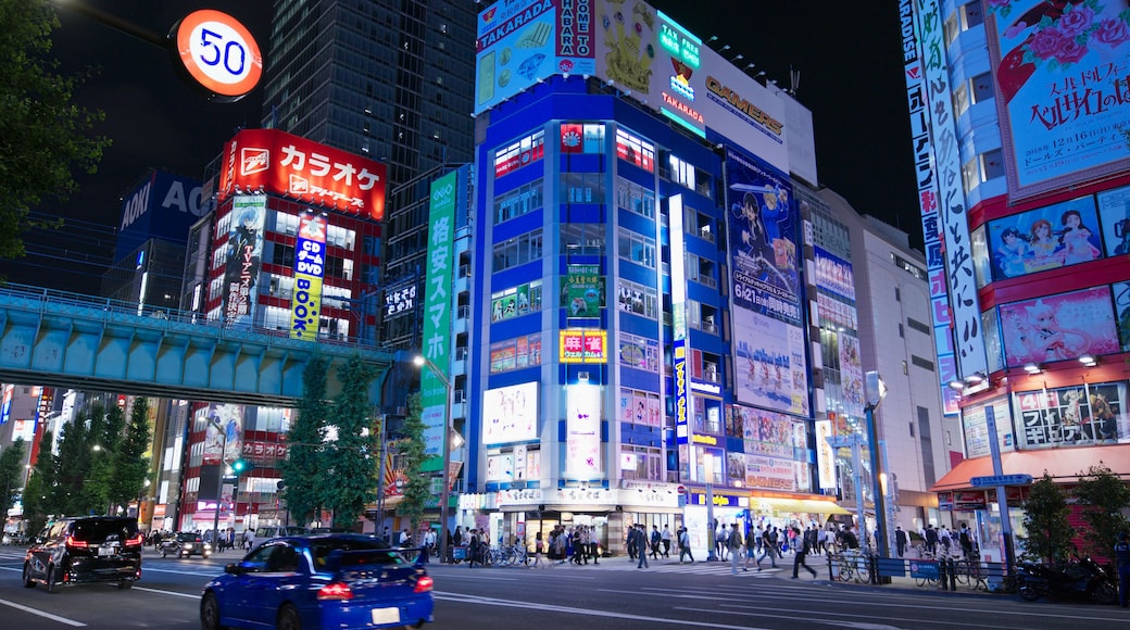 A busy urban street at night with illuminated billboards and a speed limit sign.