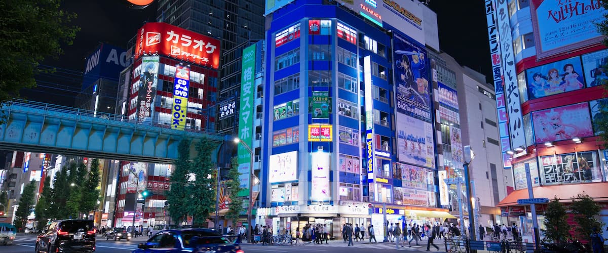 A busy urban street at night with illuminated billboards and a speed limit sign.