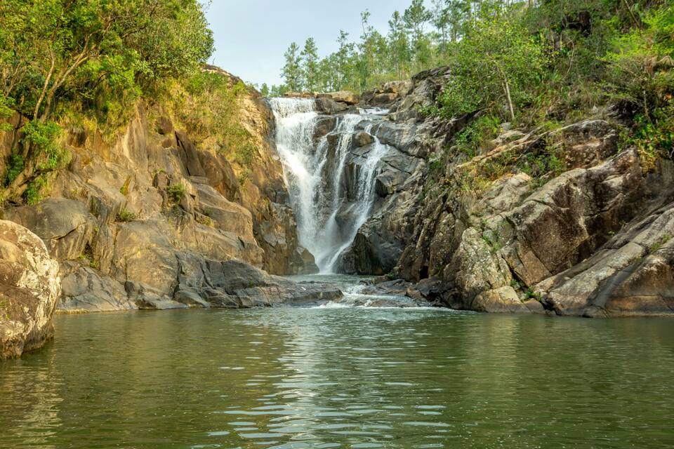 A waterfall cascading down a rocky cliff into a calm pool surrounded by lush greenery.