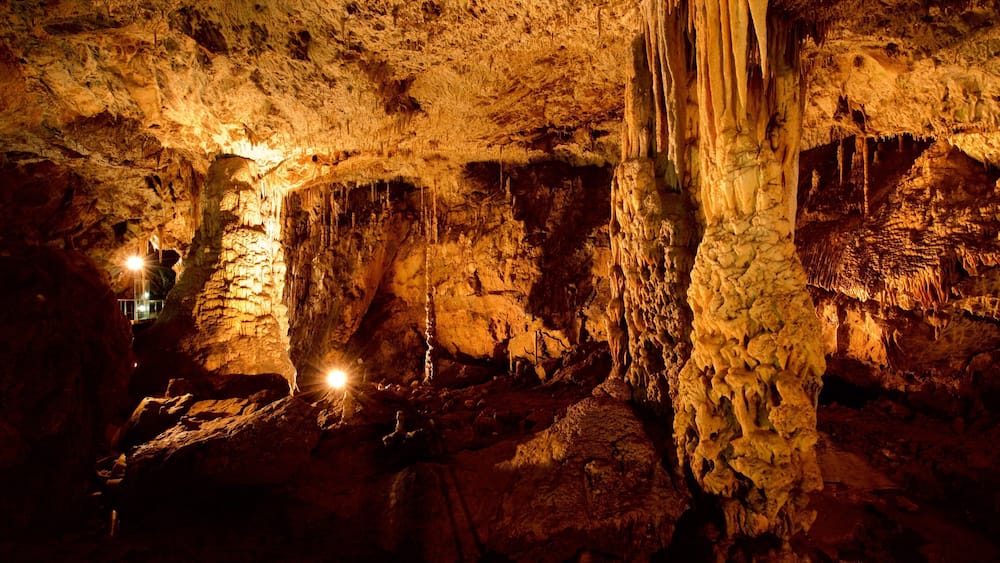 A cave with stalactites and stalagmites, illuminated by artificial lighting.