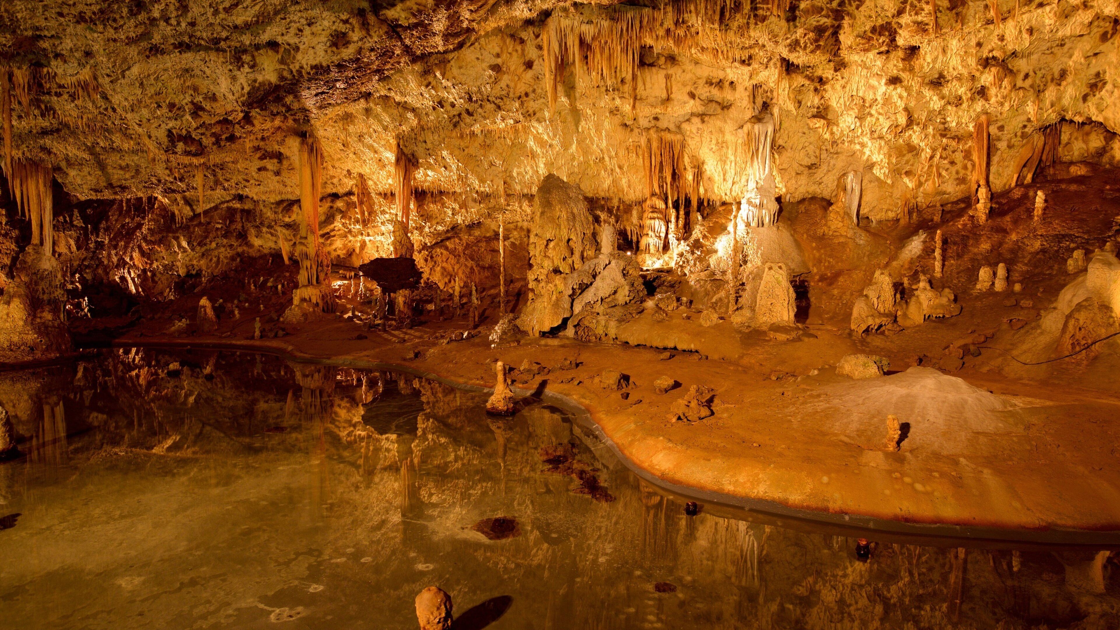 A cave with stalactites and stalagmites, a reflective pool, and a pathway.