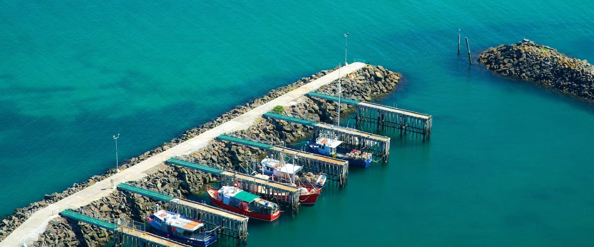 An aerial view of a pier with several boats docked, surrounded by turquoise water and rocky outcrops.