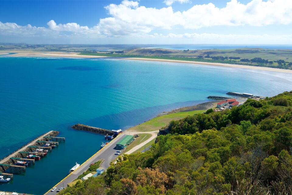 A coastal landscape with a clear blue sea, a sandy beach, and a dock with boats.