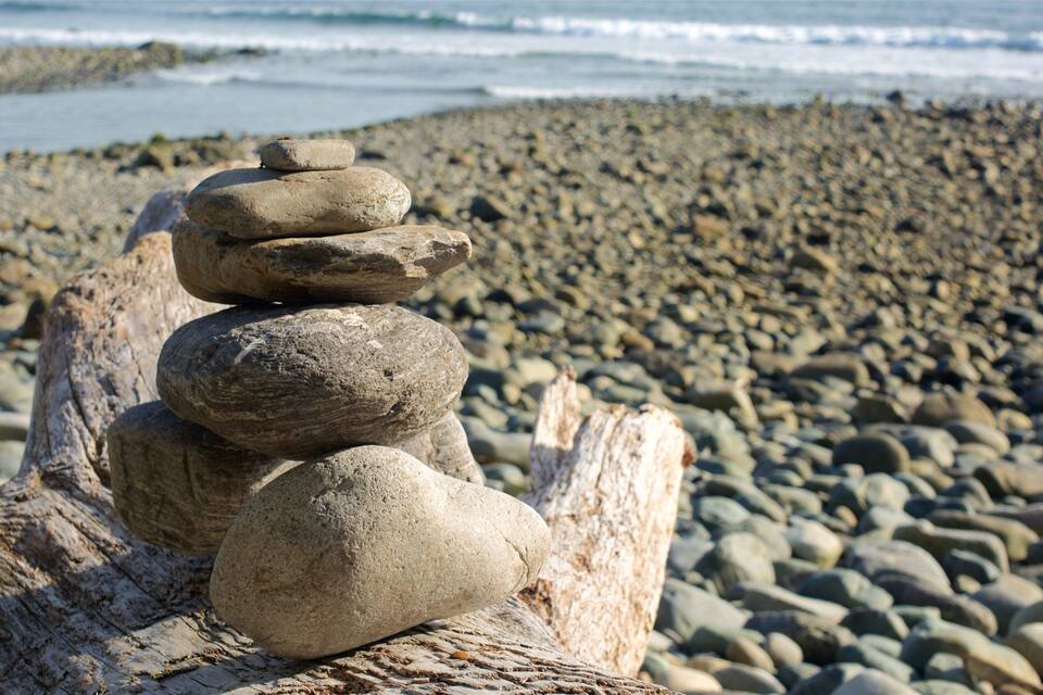 A stack of smooth, rounded stones balanced on a driftwood log by the ocean.