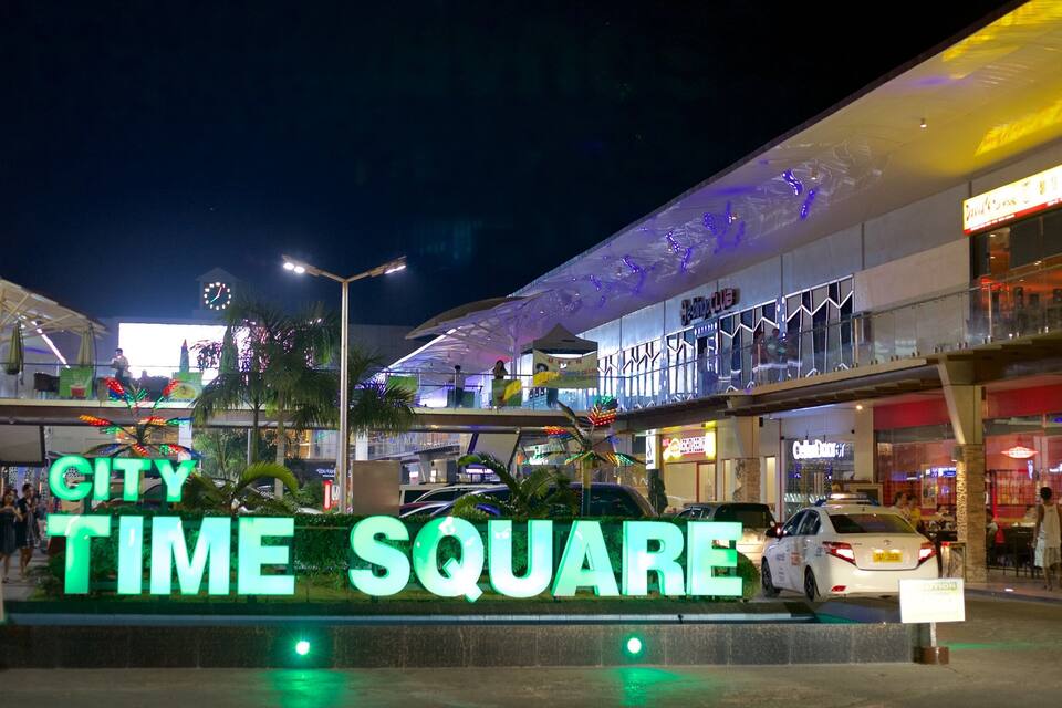 TIEMPO EN LA CIUDAD, con letreros iluminados y un centro comercial moderno al fondo.