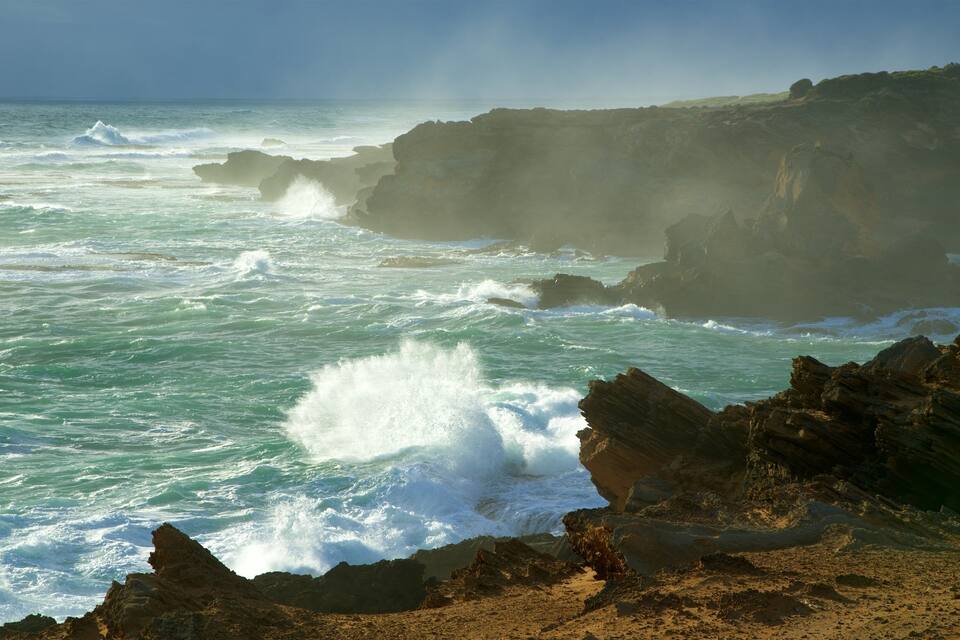 A rugged coastline with turbulent waves crashing against rocky outcrops.