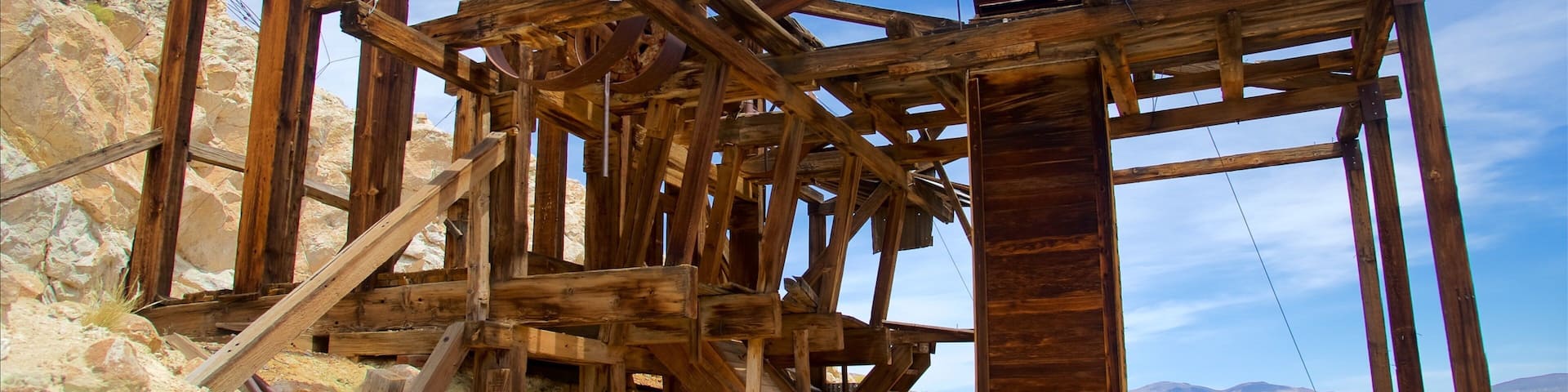 A wooden structure with a metal bell tower, surrounded by rocky terrain and mountains.