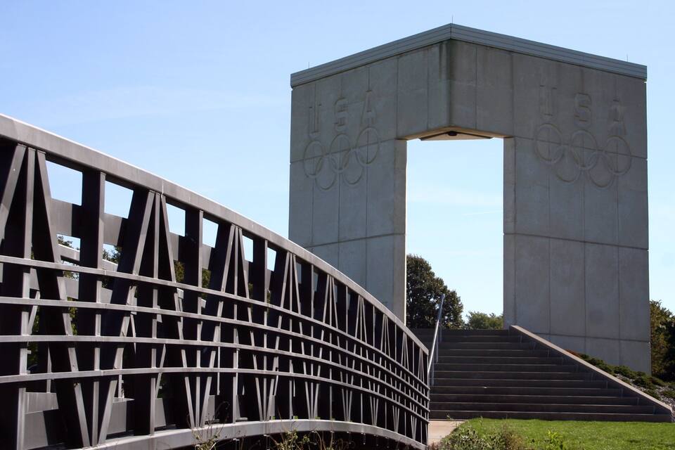 Un gran arco de hormigón con aros olímpicos y una escalera que lleva hacia él.