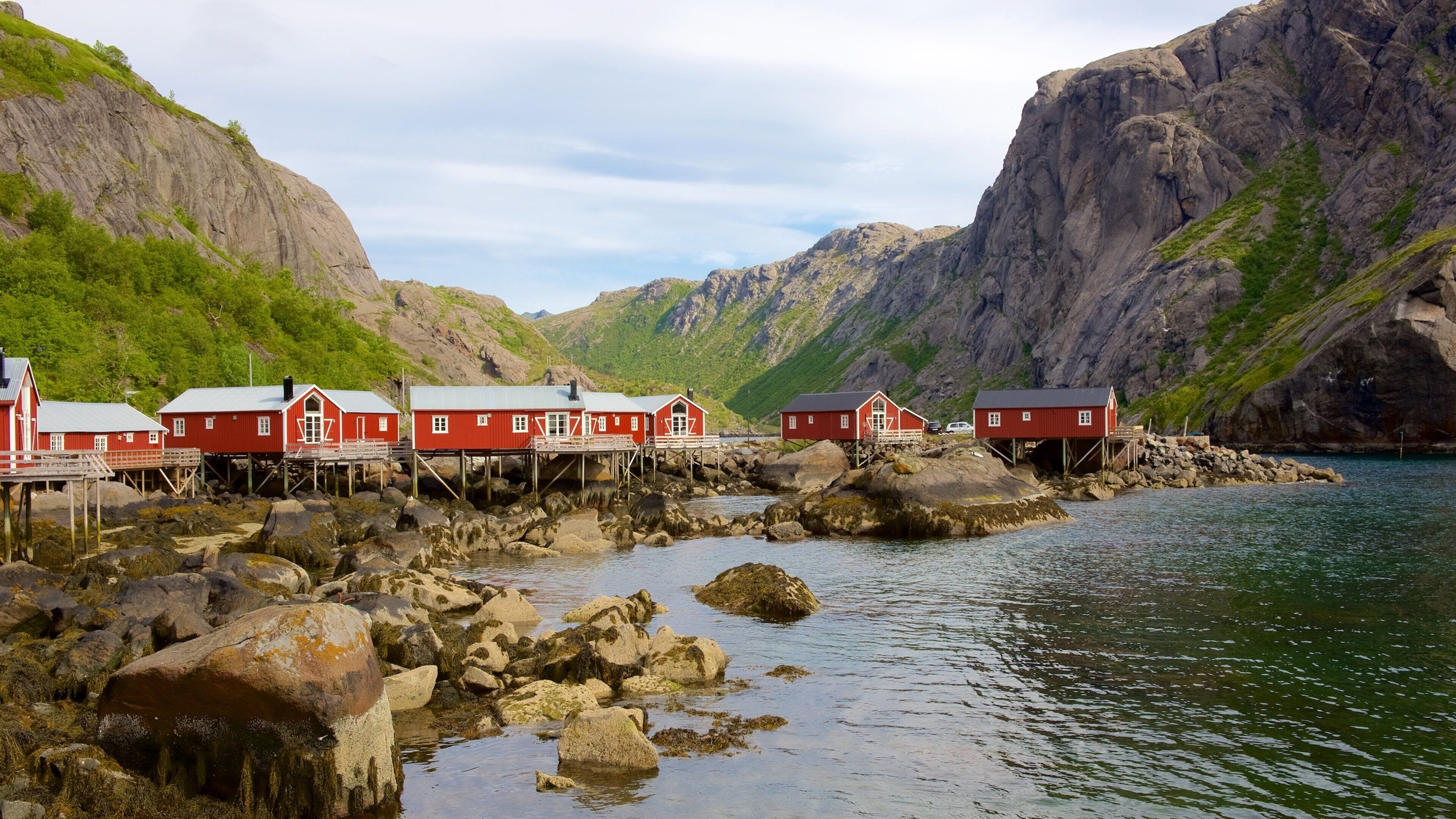 A coastal village with red buildings on stilts by the sea, surrounded by rocky cliffs and greenery.