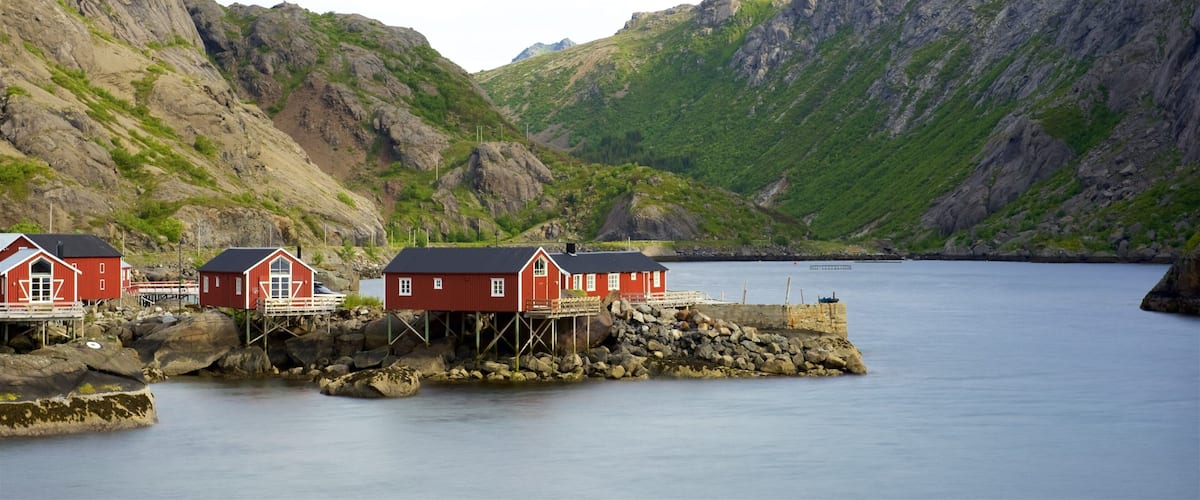 A coastal village with red houses on stilts by a calm sea, surrounded by rocky cliffs.